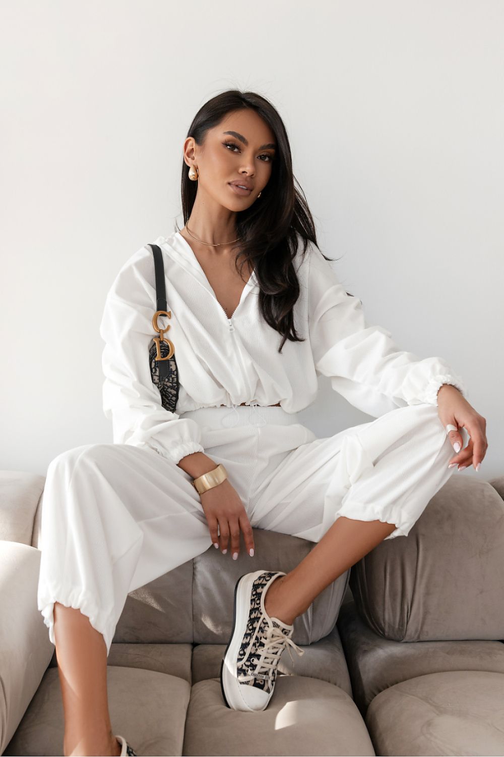 Woman in a white outfit sitting on a couch with a neutral background