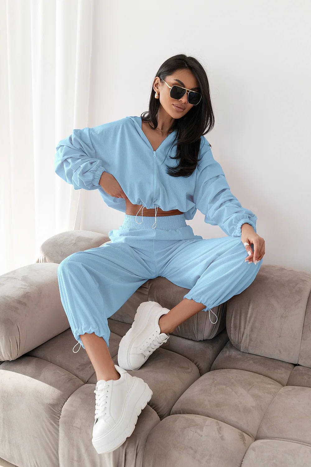 Woman in a light blue outfit sitting on a beige sofa.