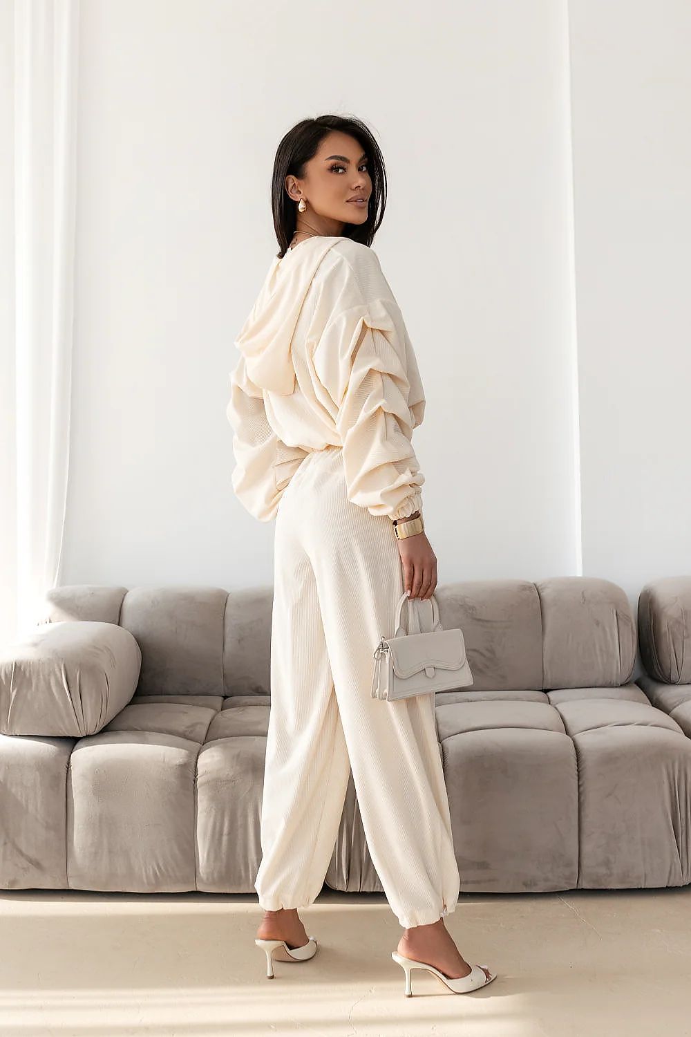 Woman in a white outfit standing in a living room with a gray sofa.