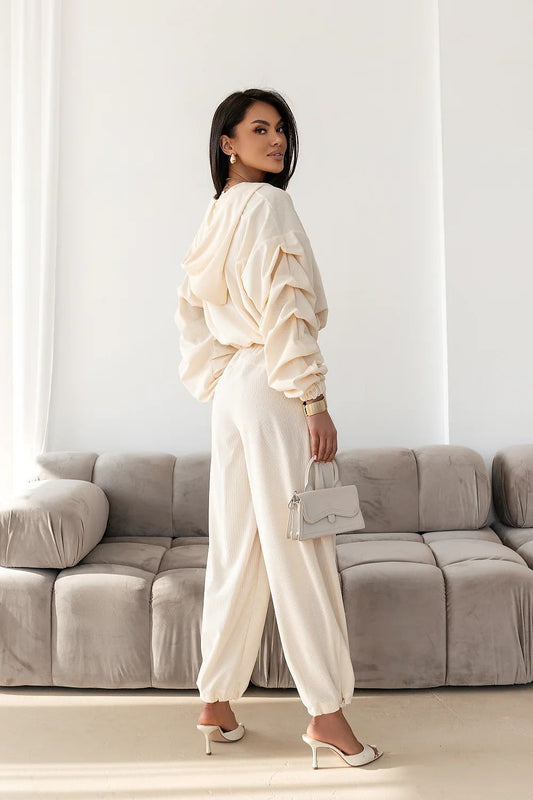 Woman in a white outfit standing in a living room with a gray sofa.