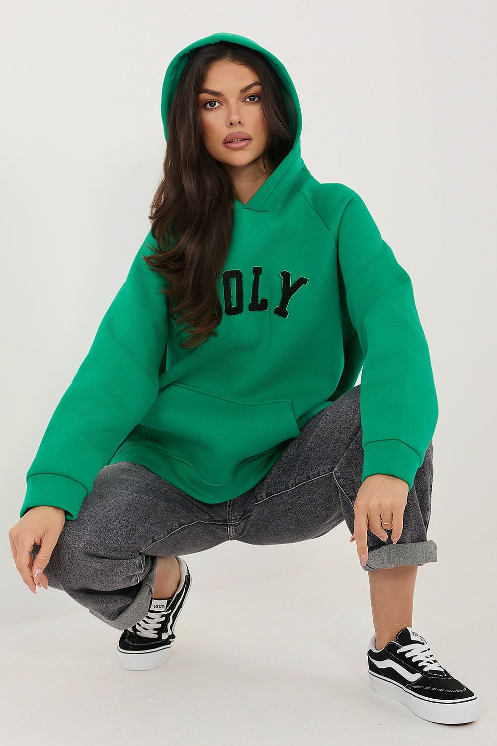Woman wearing a green hoodie with text, gray pants, and black and white sneakers on a white background