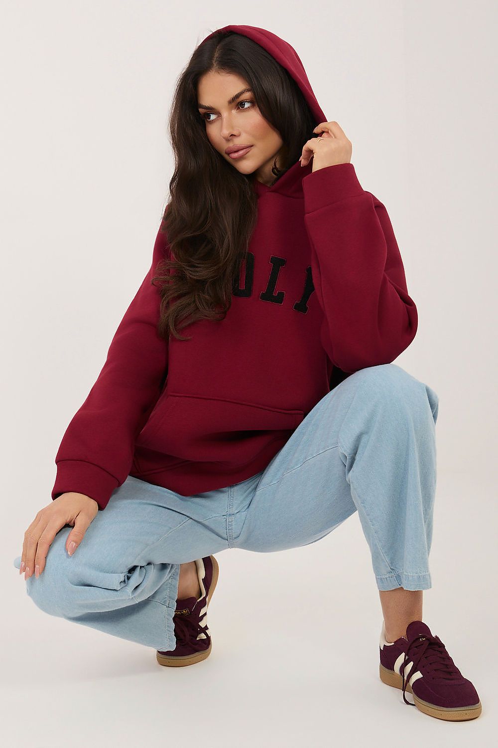 Woman wearing a red hoodie with text, light blue jeans, and maroon sneakers on a white background