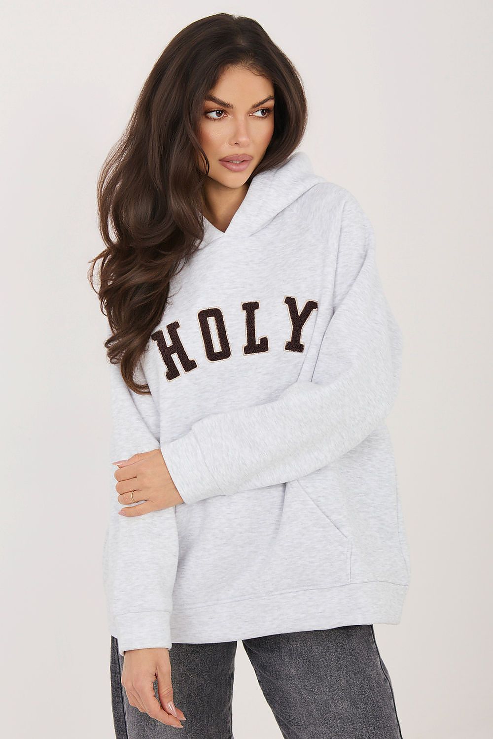 Woman wearing a gray hoodie with 'HOLY' text on a plain background