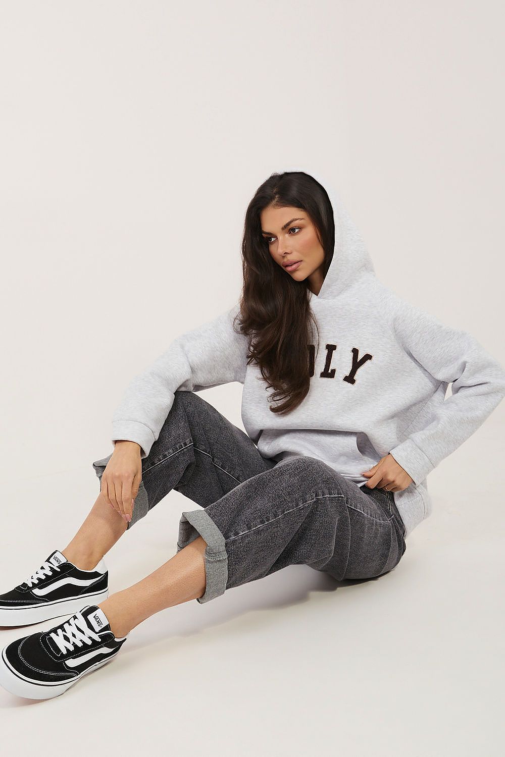 Woman wearing a light gray hoodie with 'LY' on it, sitting on a white floor.