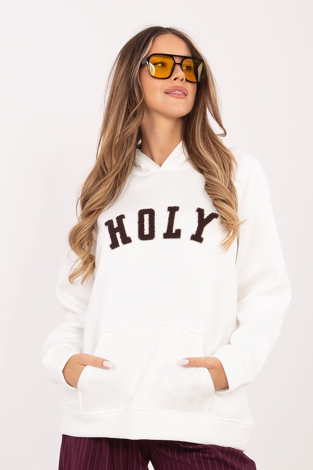 Woman wearing a white hoodie with 'HOLY' text and sunglasses on a white background