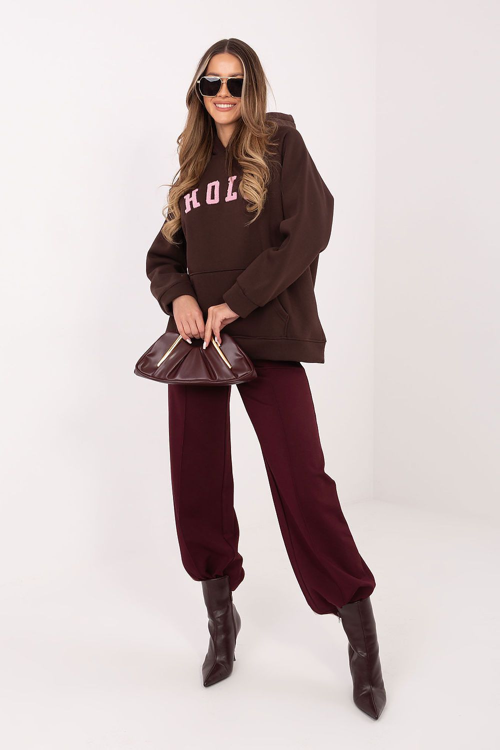 Woman wearing a brown oversized sweater, burgundy pants, and black boots on a white background