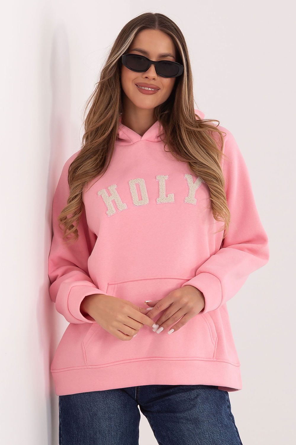 Woman wearing a pink hoodie with 'HOLY' text on a white background