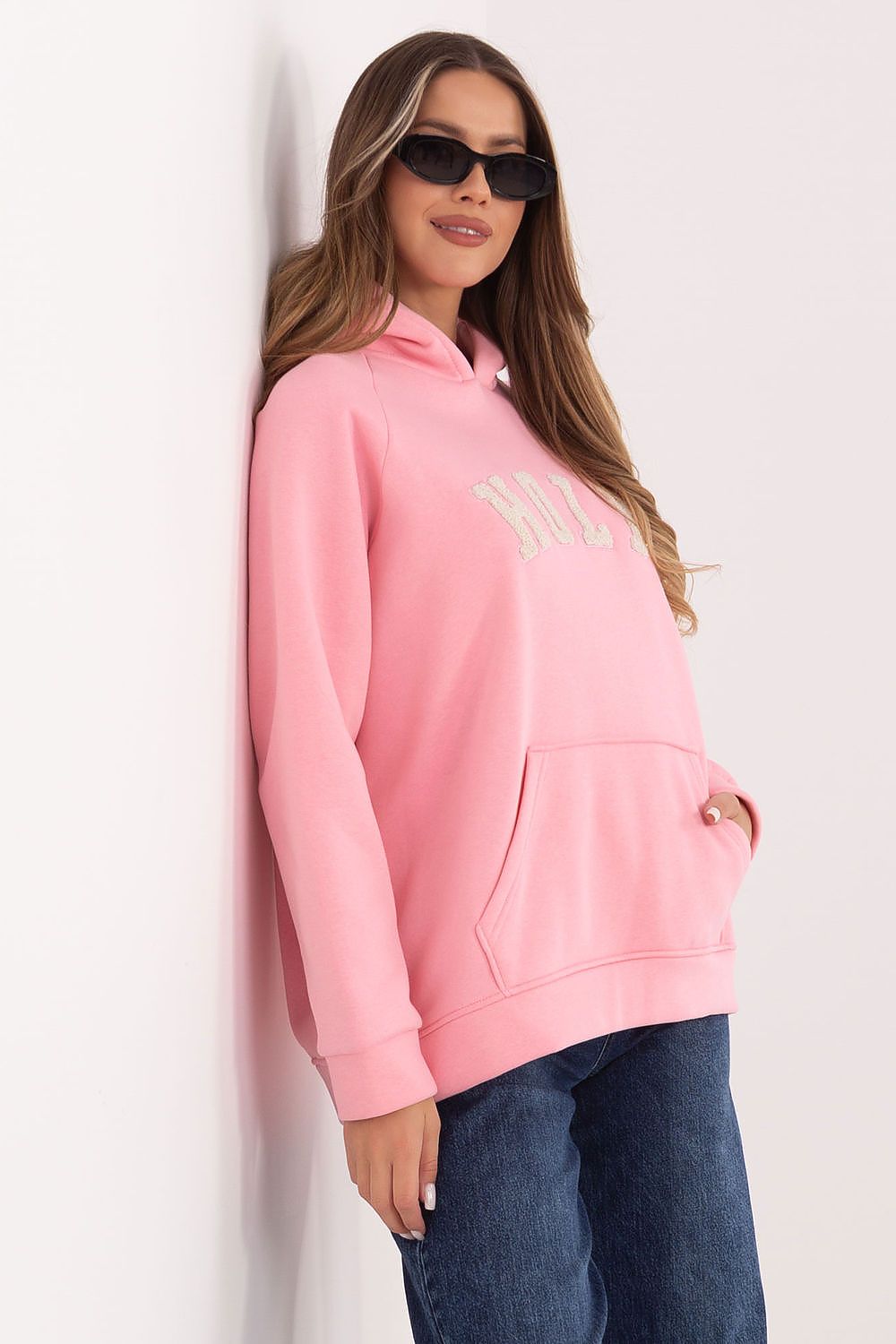 Woman wearing a pink hoodie with a brand logo against a white background