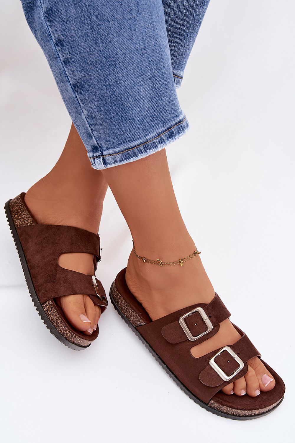 Brown sandals with buckles worn with blue jeans on a white background