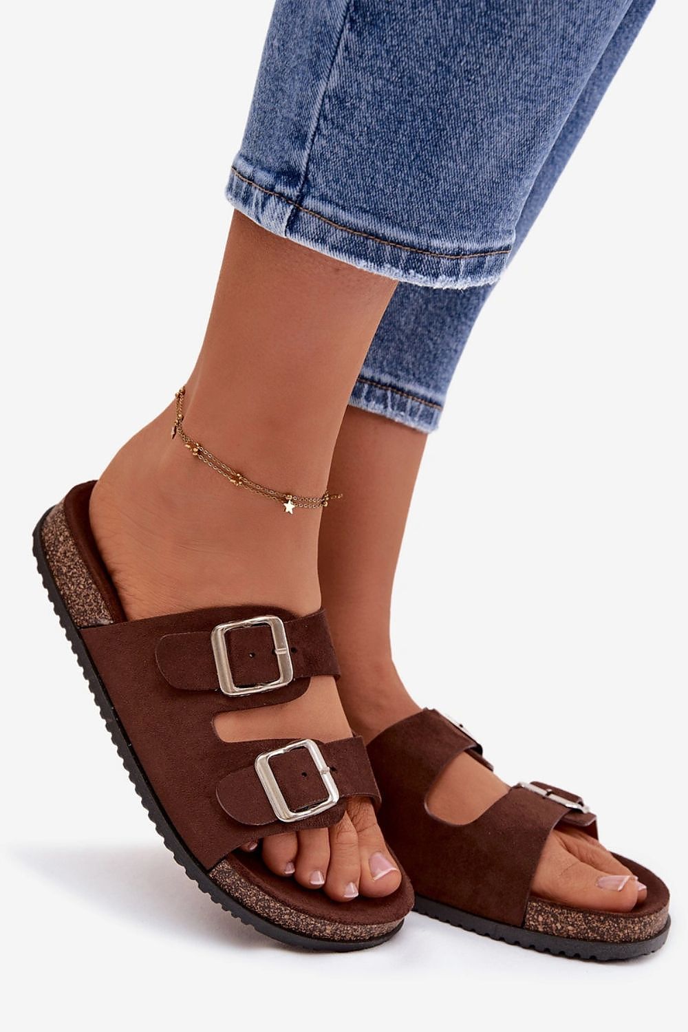 Brown sandals with buckles worn with blue jeans on a white background