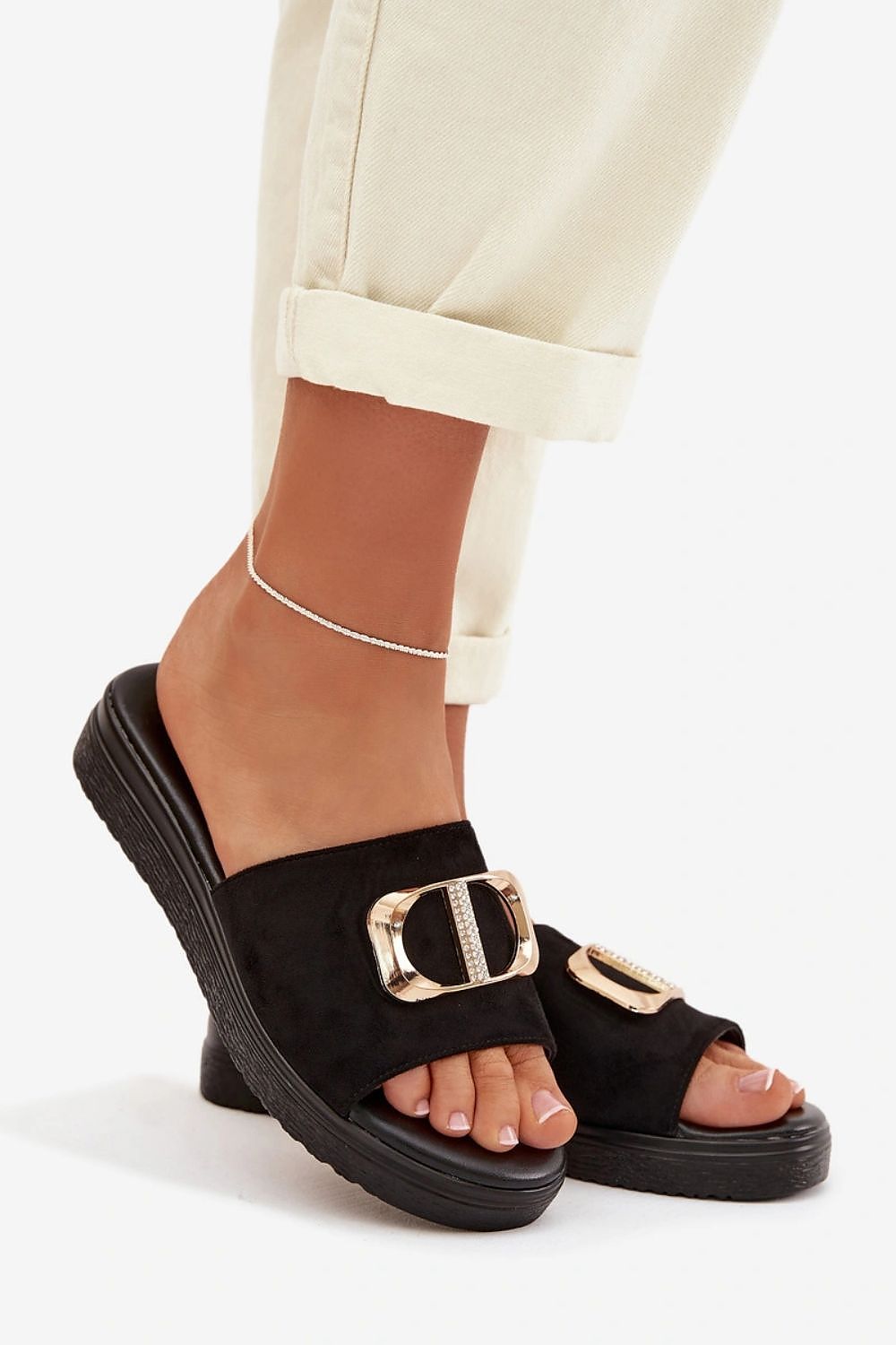 Black sandals with gold buckles worn by a person on a white background