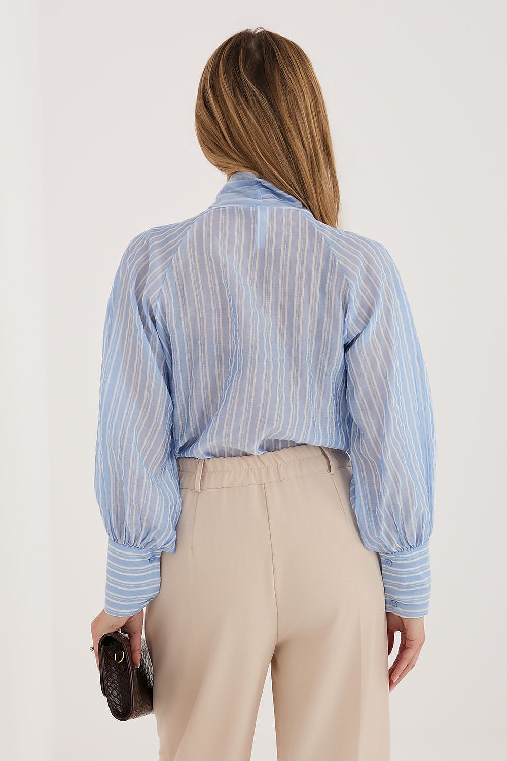 Woman wearing a light blue striped shirt and beige pants against a white background