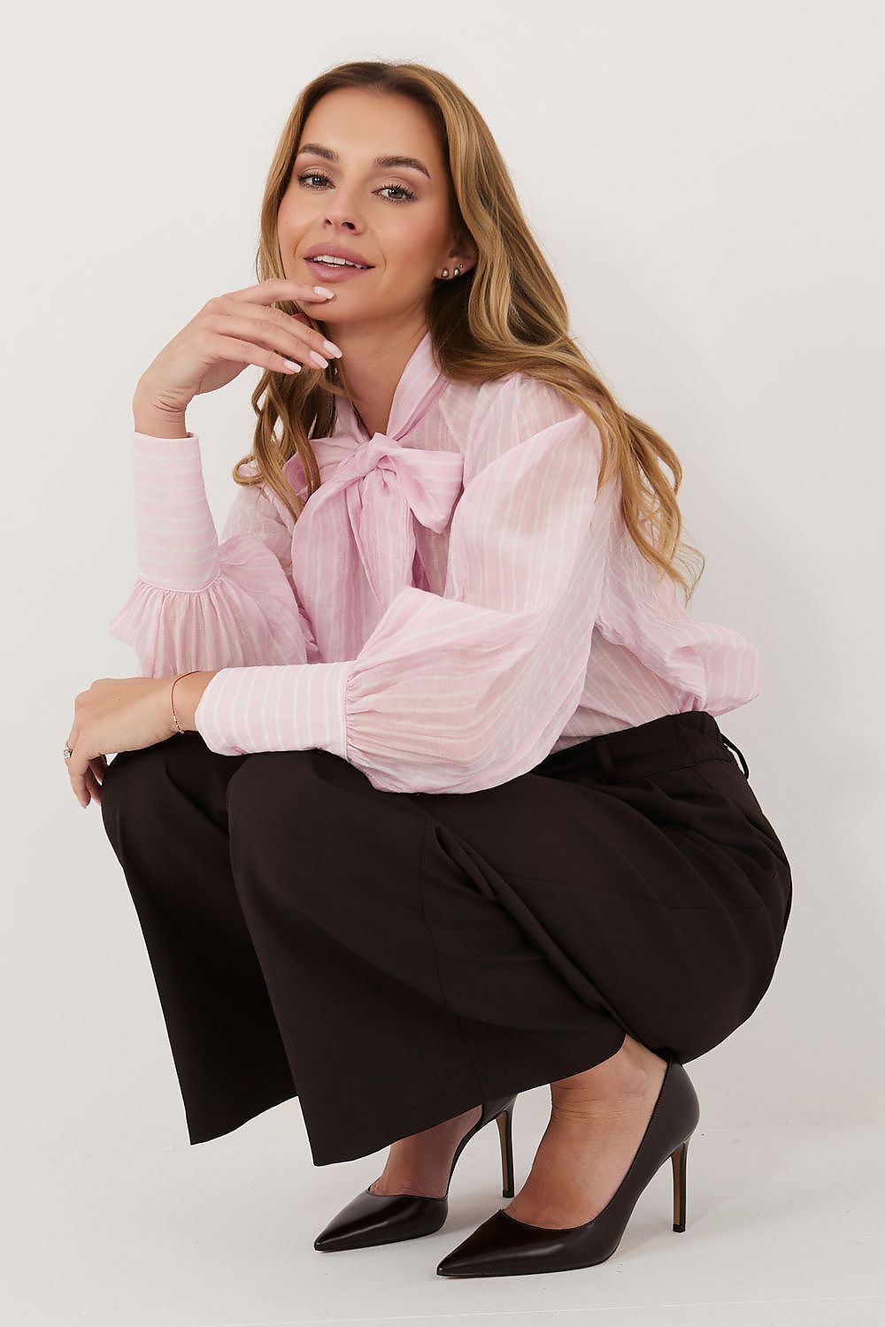 Woman wearing a pink blouse with a bow and black pants on a white background