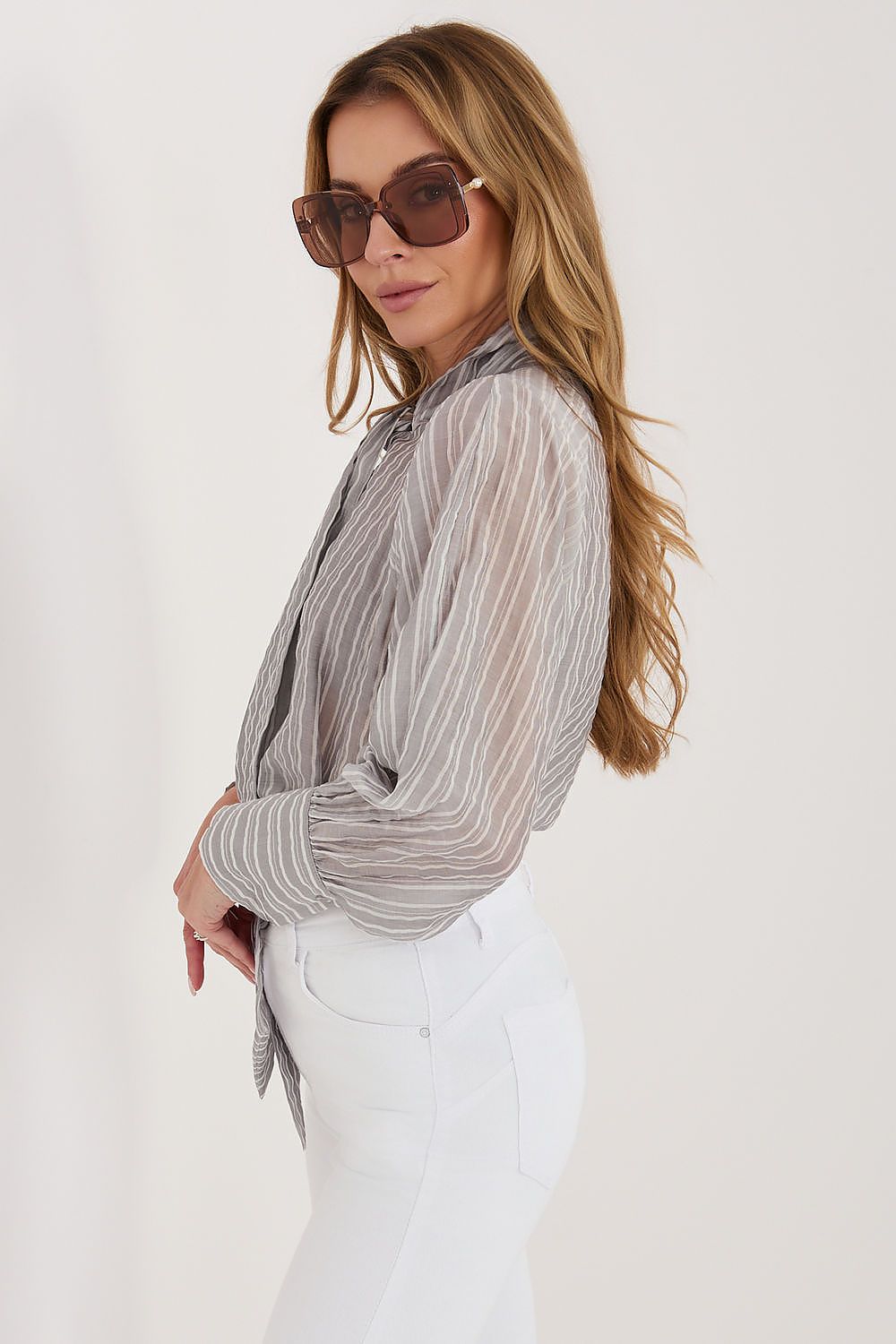 Woman wearing a sheer striped shirt and sunglasses on a white background