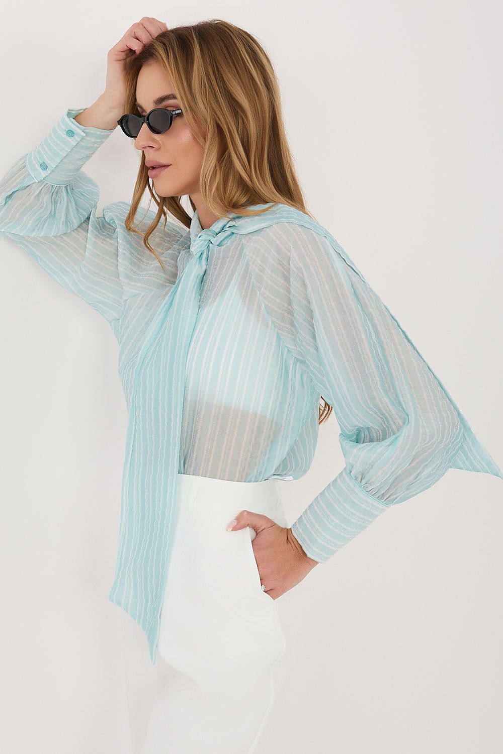 Woman wearing a light blue sheer blouse with a white background