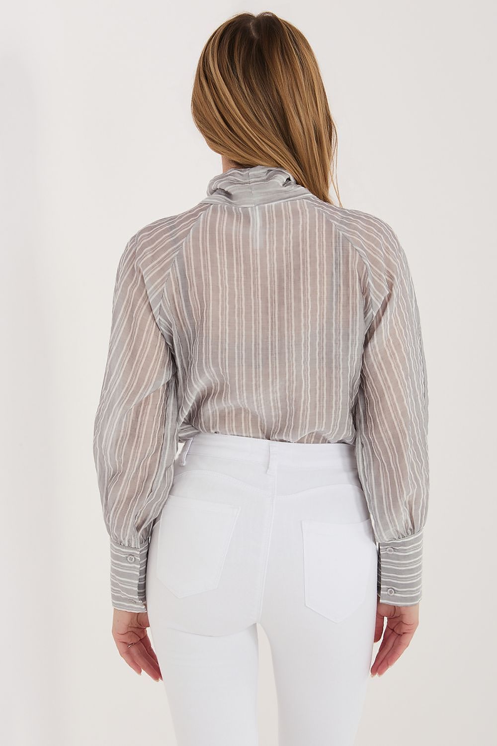 Woman wearing a striped shirt and white pants on a plain background