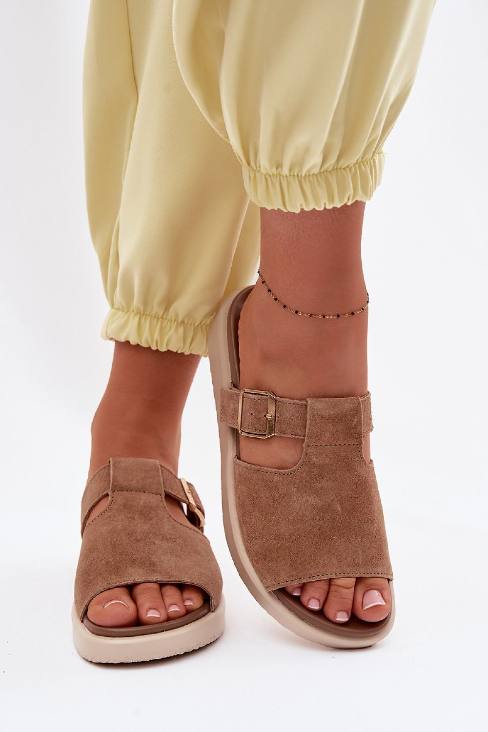 Brown open-toe sandals worn with yellow pants on a white background