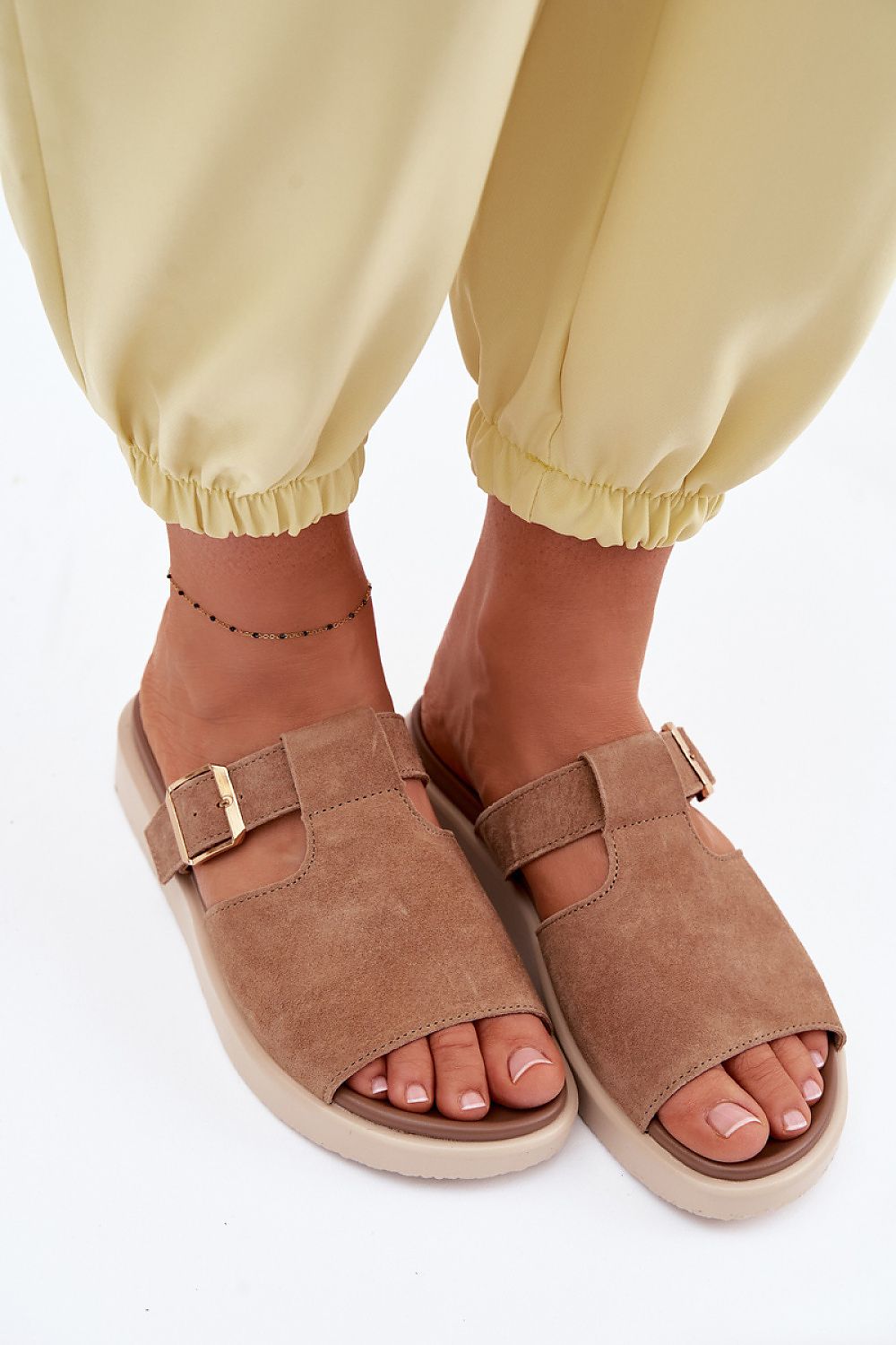 Brown suede sandals worn with yellow pants on a white background