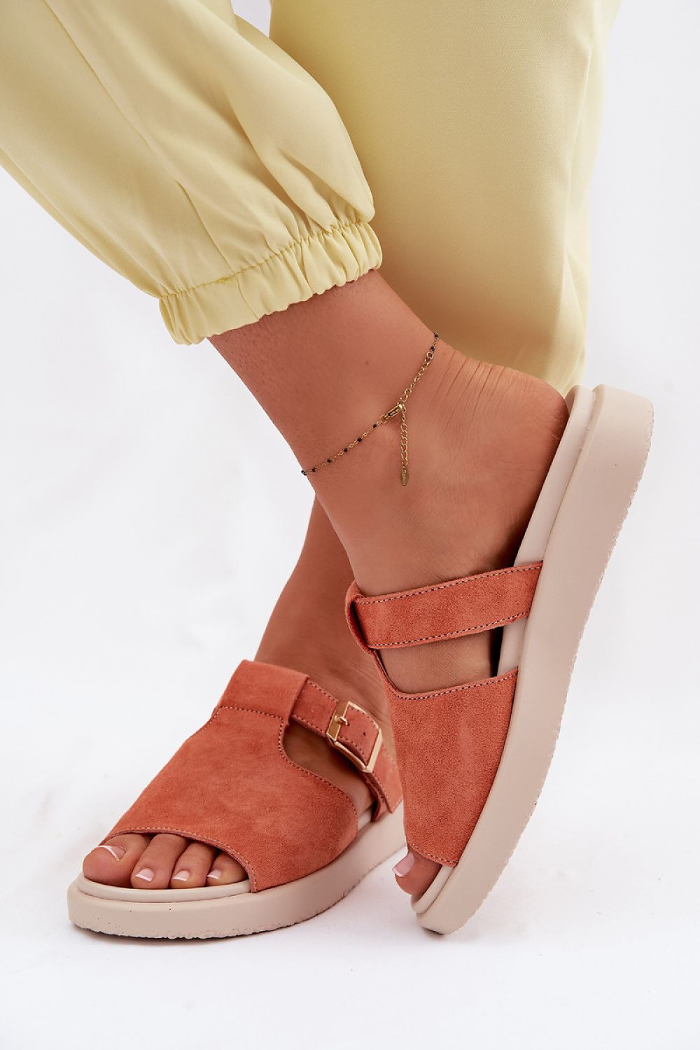 Orange sandals worn with yellow pants on a white background