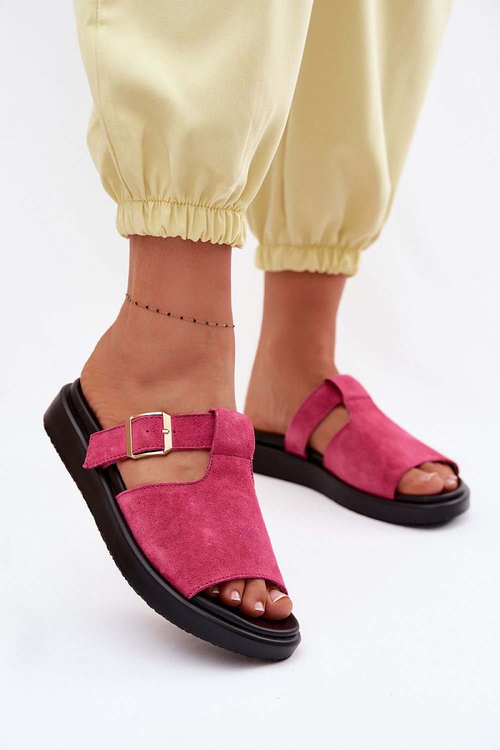 Pink sandals worn with yellow pants on a white background