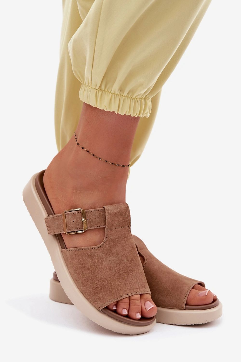 Brown open-toe sandals worn with yellow pants on a white background