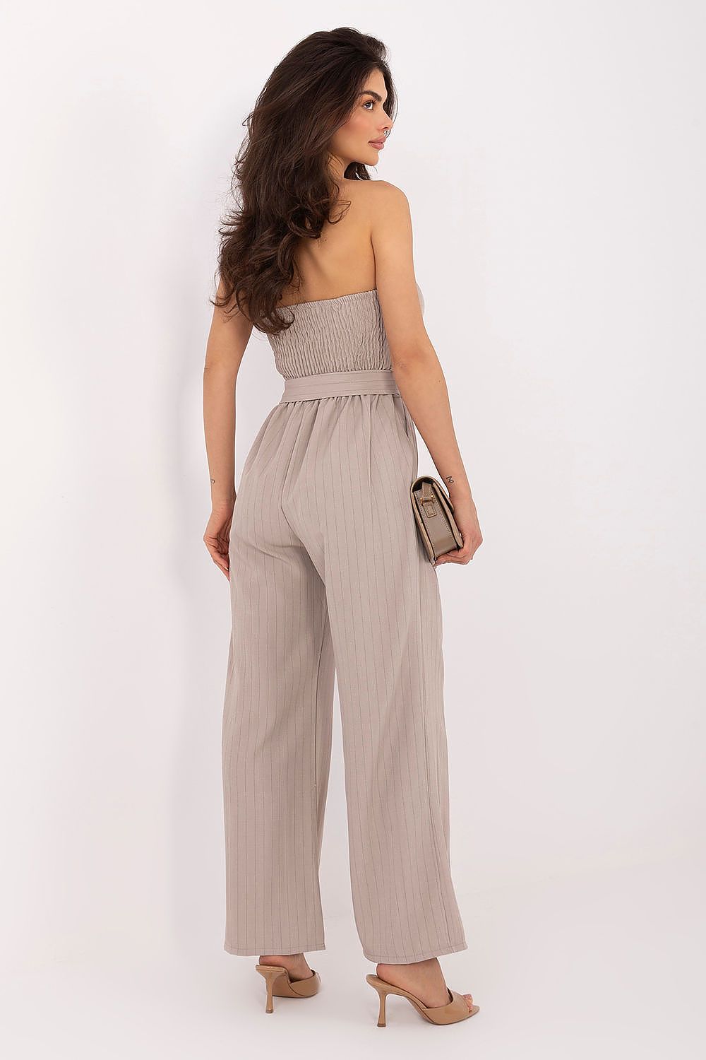 Woman wearing a beige strapless jumpsuit against a white background