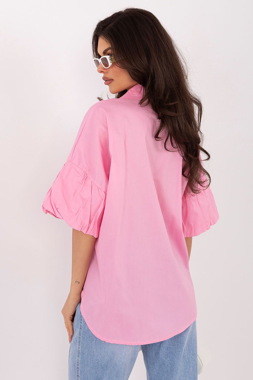 Woman wearing a pink shirt and blue jeans against a white background