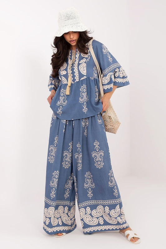 Woman wearing a blue embroidered outfit with white patterns on a white background
