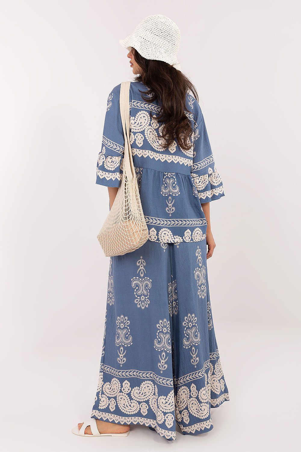 Woman wearing a blue and white patterned dress with a white beanie and bag on a white background