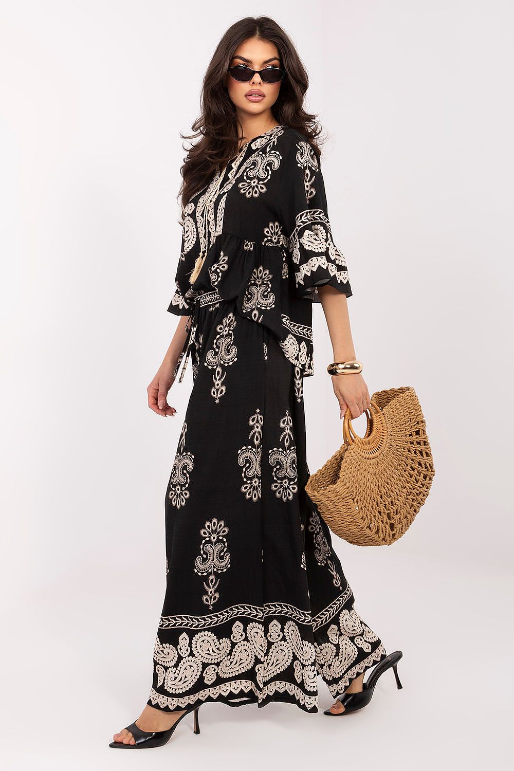 Woman wearing a black and white patterned outfit with a straw bag on a white background