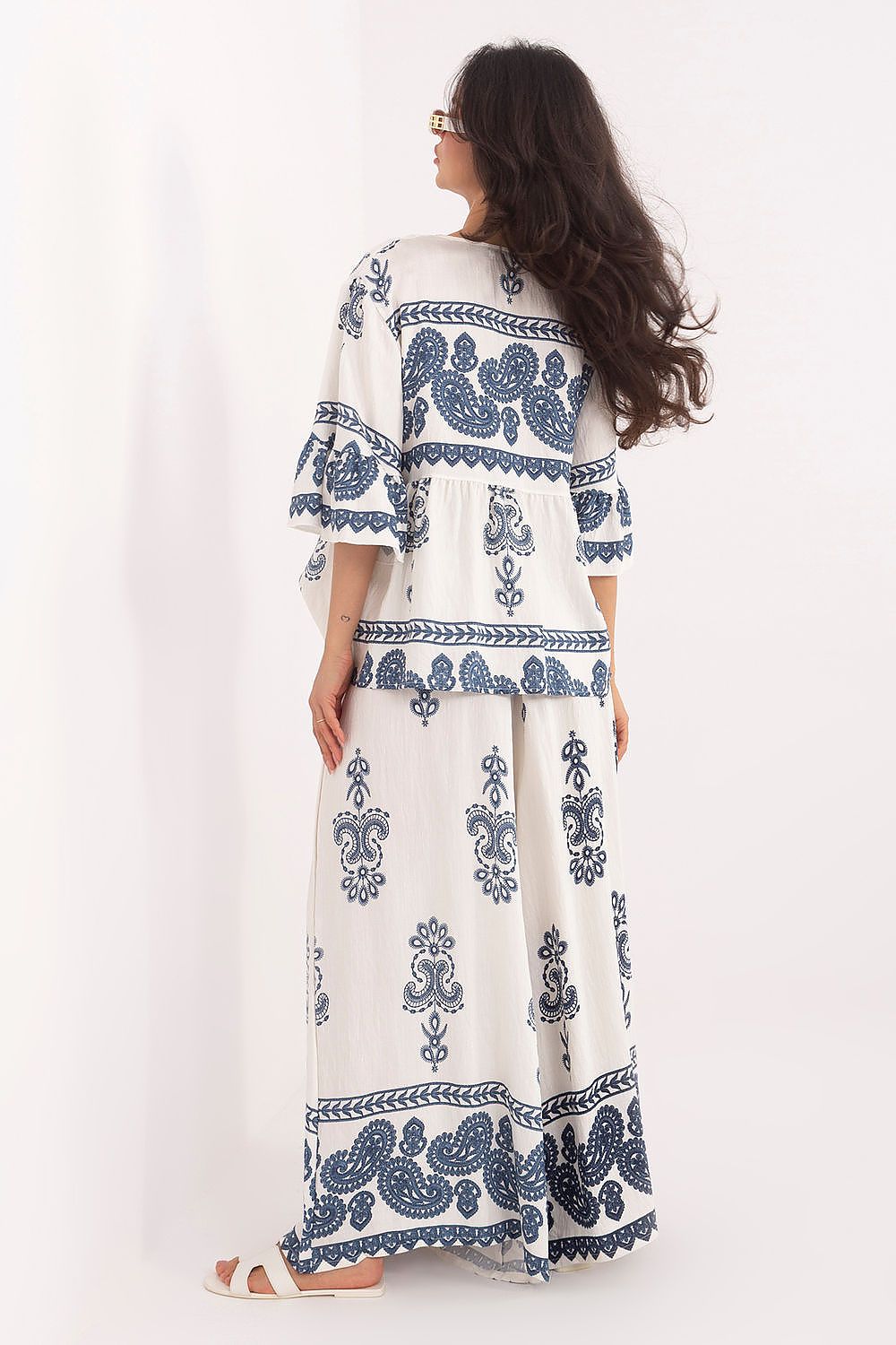 Woman wearing a long white dress with blue patterns on a white background