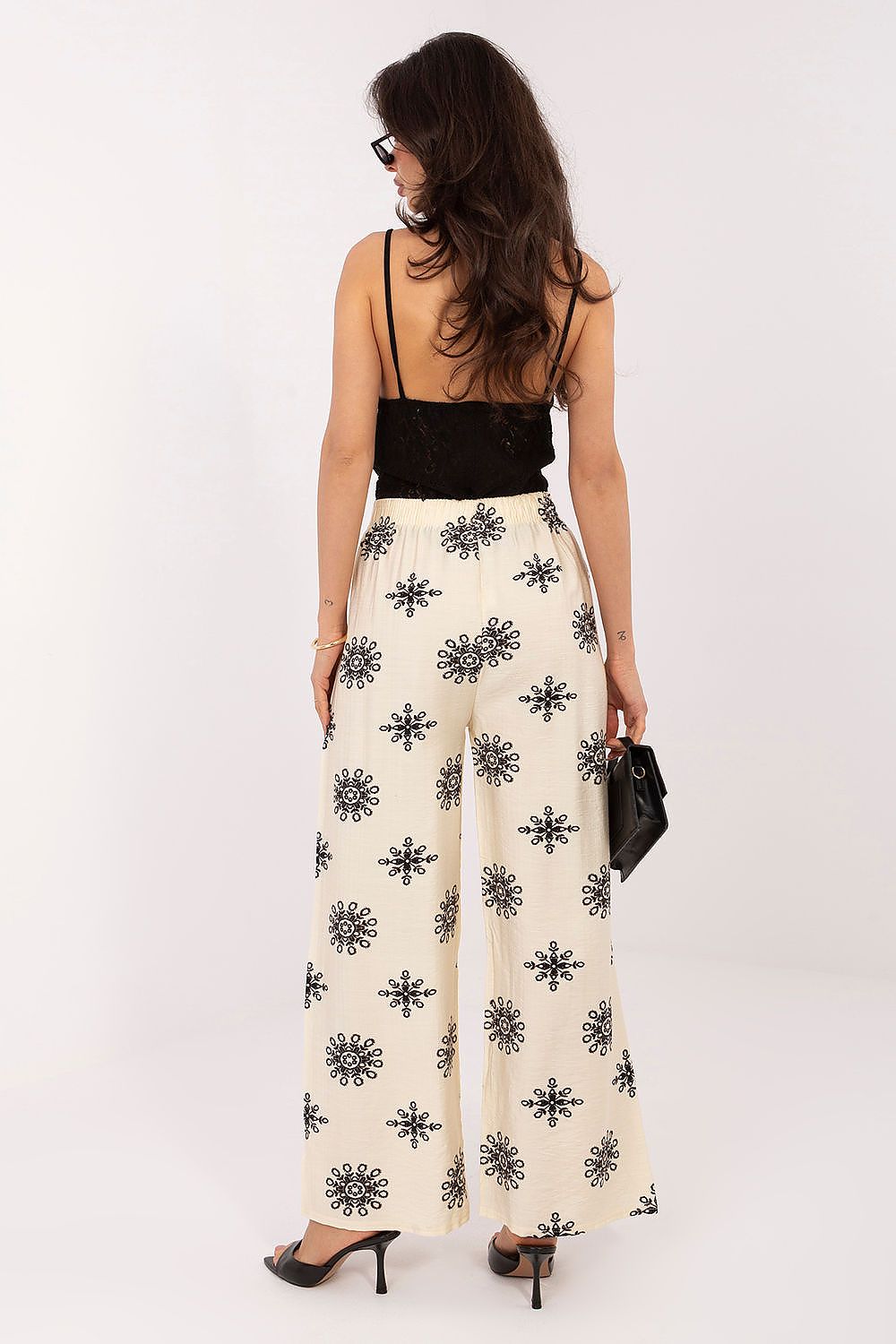 Woman wearing a black top and white pants with black patterns on a white background