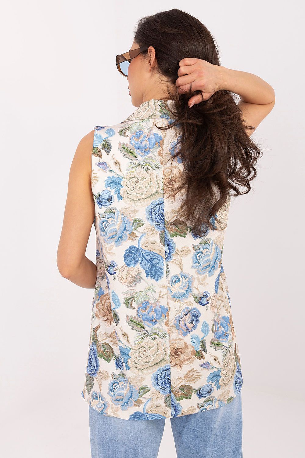 Woman wearing a sleeveless floral top with blue and beige flowers on a white background