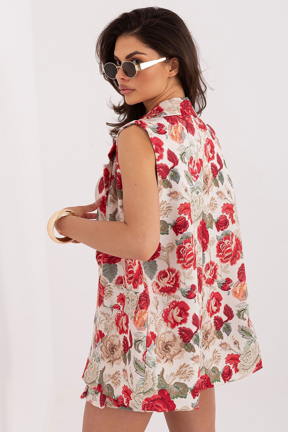 Woman wearing a sleeveless floral dress with red and beige flowers on a white background