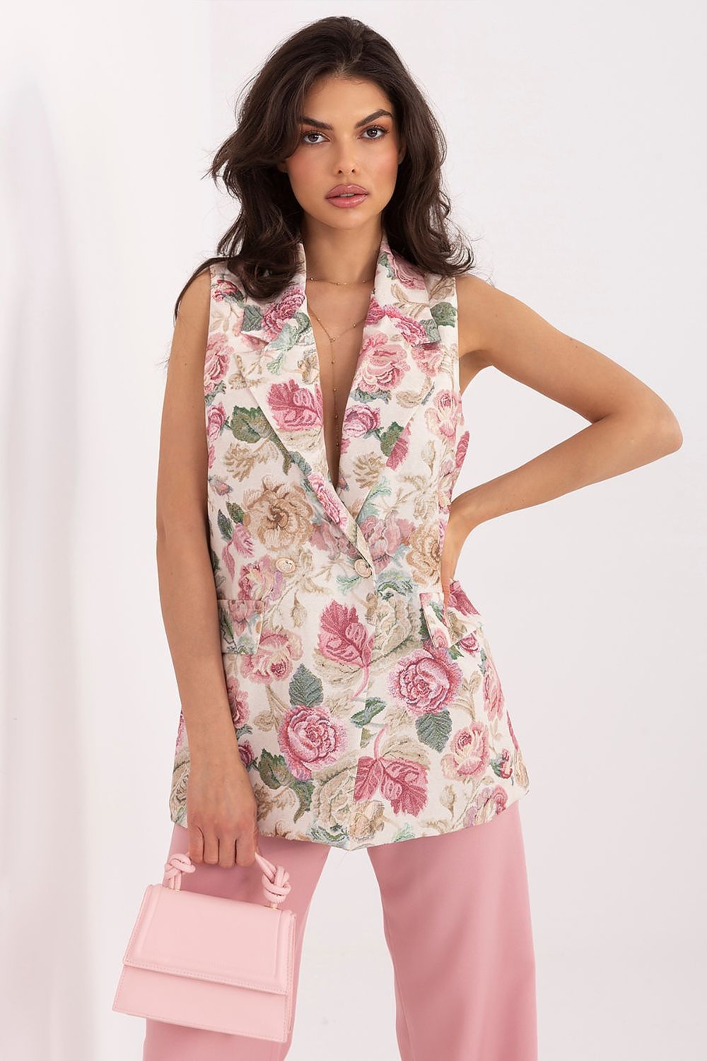 Woman wearing a floral sleeveless top and pink pants with a white background