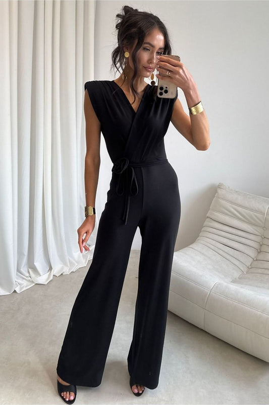 Woman taking a mirror selfie wearing a black jumpsuit in a minimalistic room.