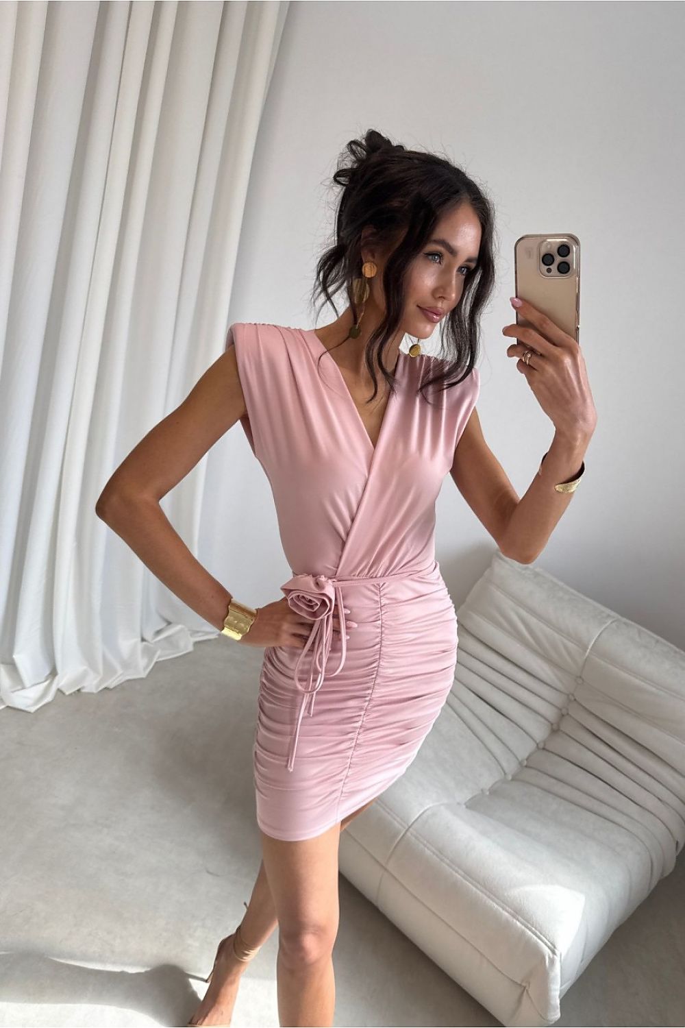 Woman taking a mirror selfie wearing a pink dress in a minimalistic room.