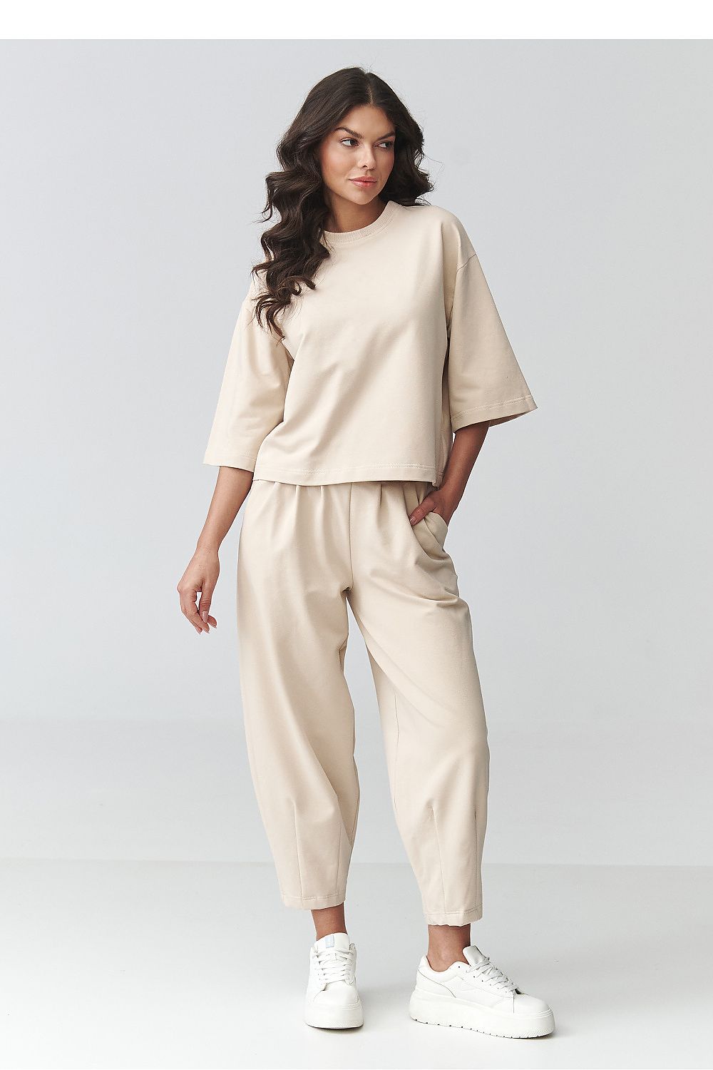 Woman wearing a beige outfit with white sneakers on a plain background