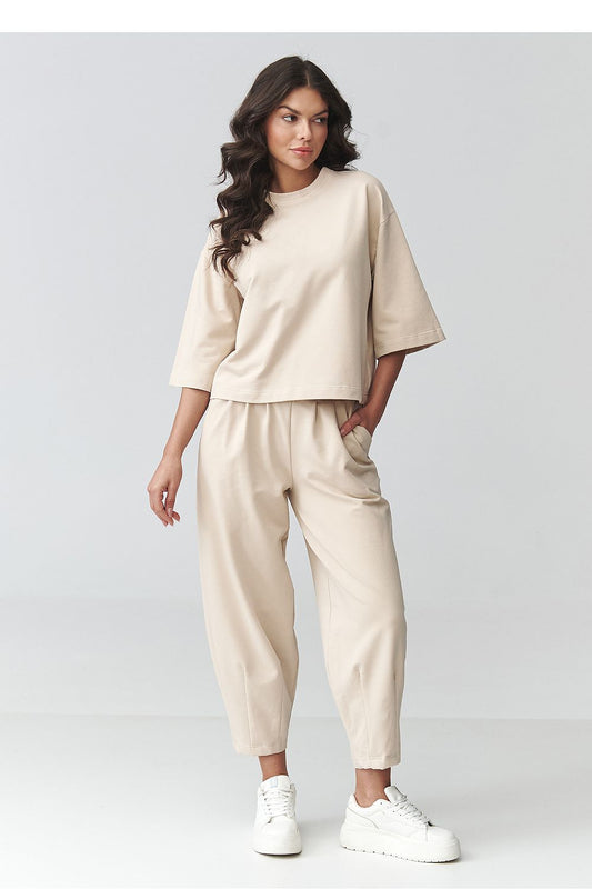 Woman wearing a beige outfit with white sneakers on a plain background