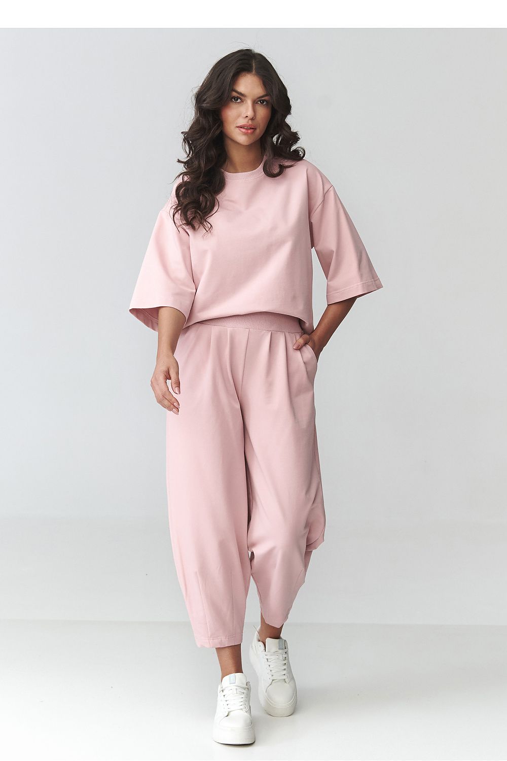 Woman wearing a pink outfit with white sneakers on a light gray background