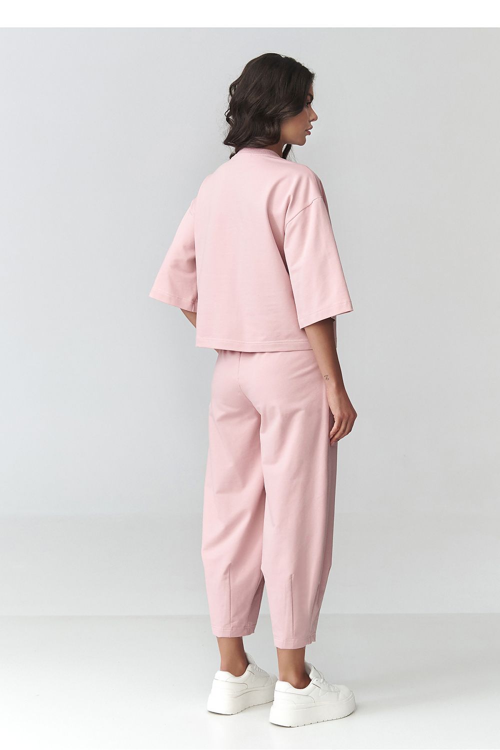 Person wearing a pink outfit with white sneakers on a light gray background
