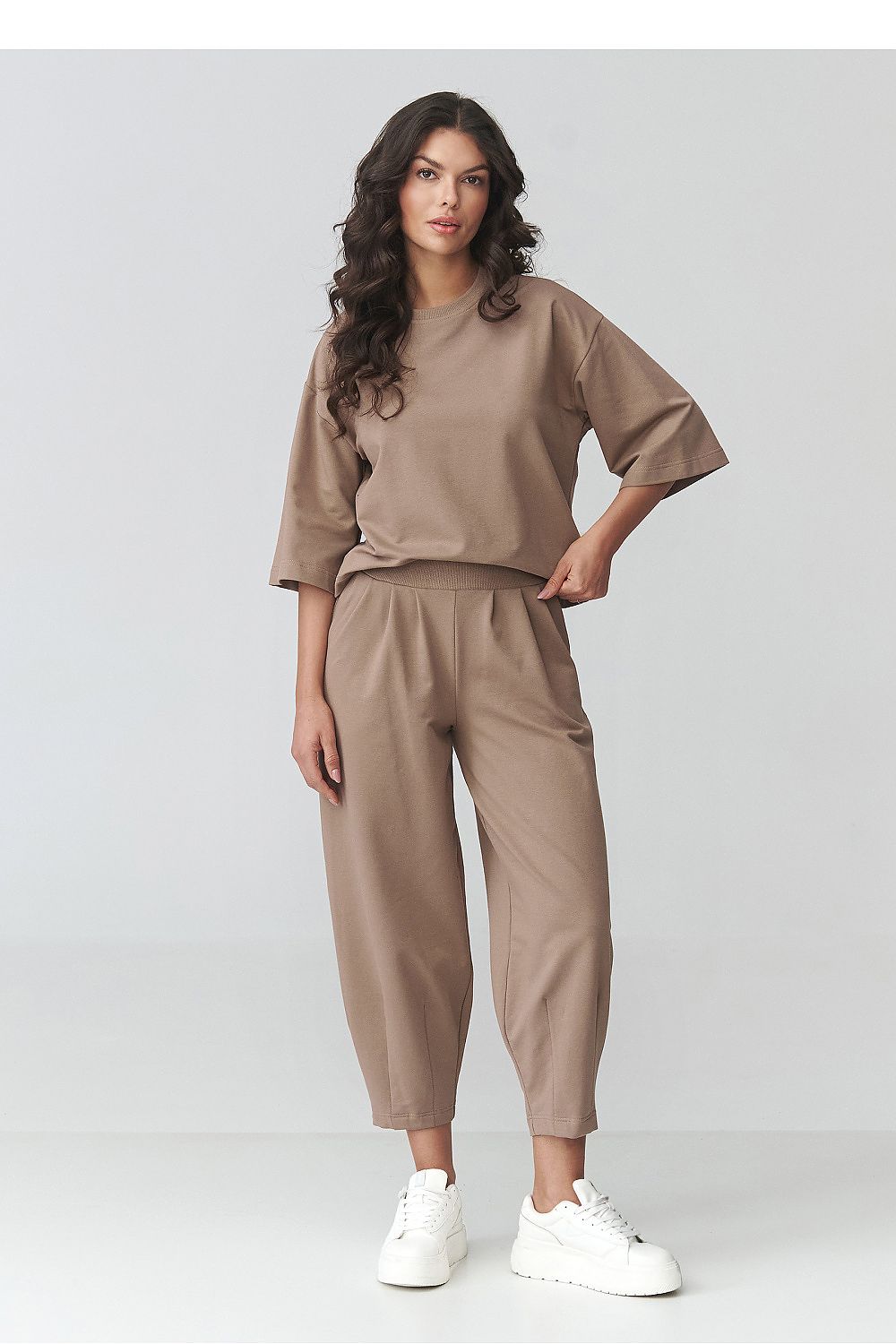 Woman wearing a beige outfit with white sneakers on a light gray background