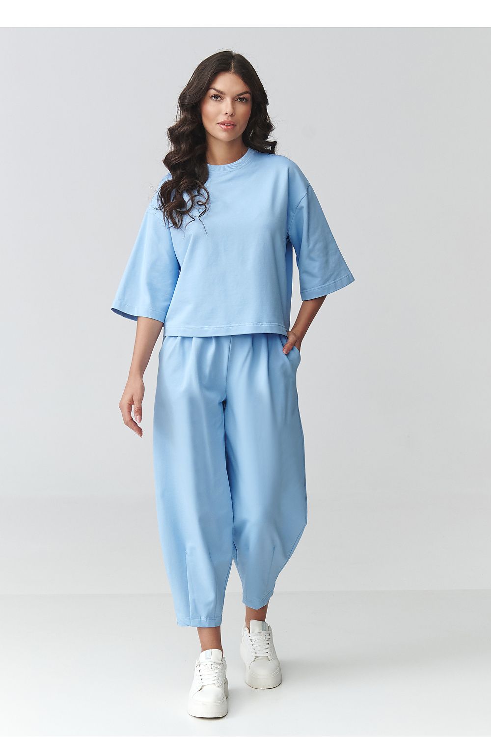 Woman wearing a light blue outfit with white sneakers on a plain background