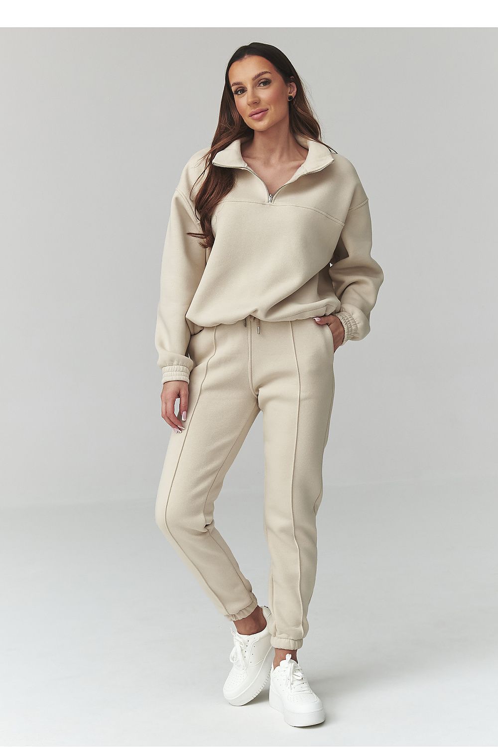 Woman wearing a beige outfit with white sneakers on a light gray background