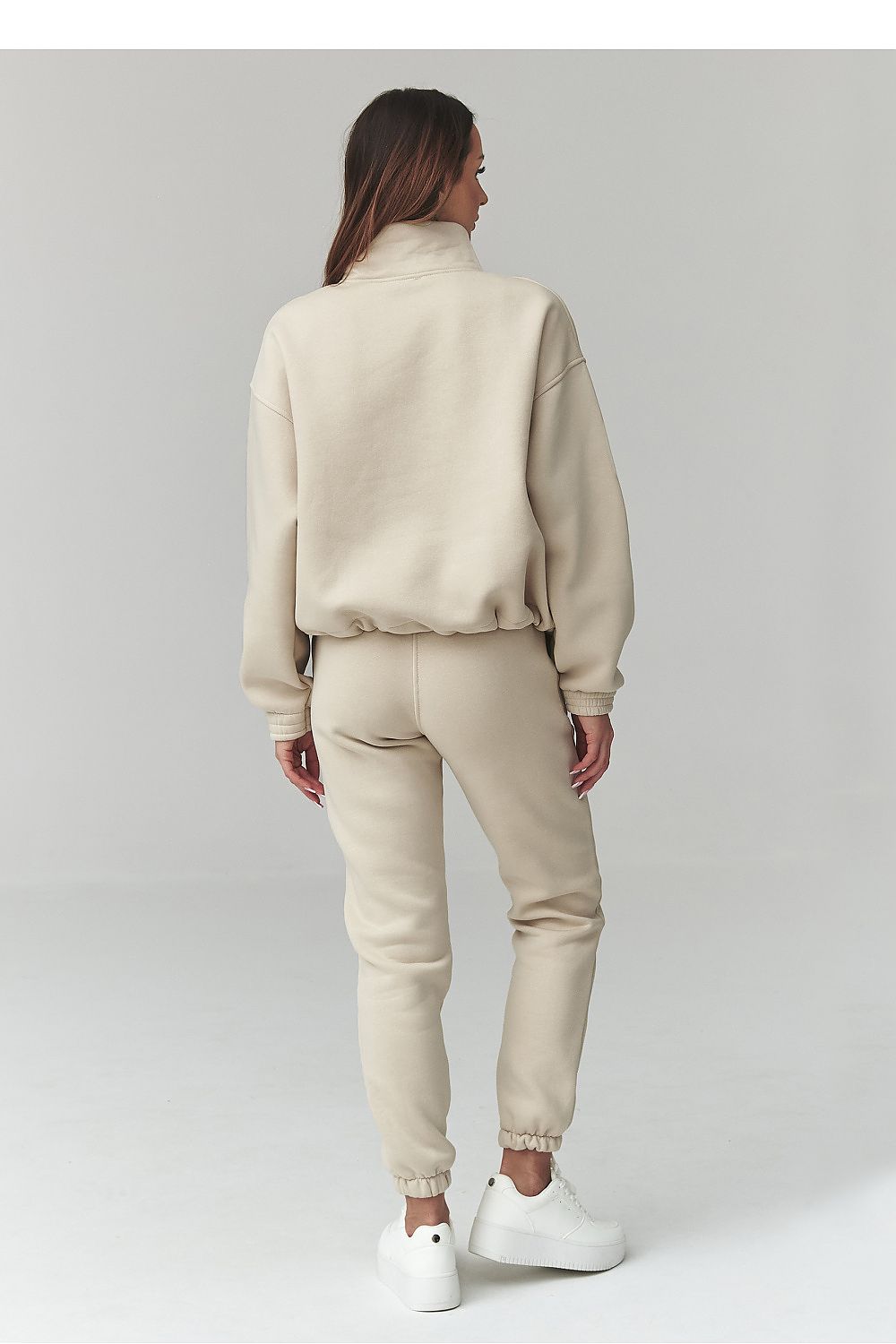 Person wearing a beige tracksuit with white shoes on a light gray background