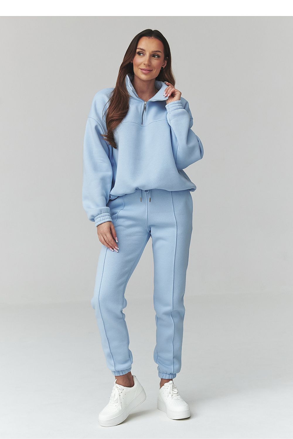 Woman wearing a light blue tracksuit with white shoes on a plain background