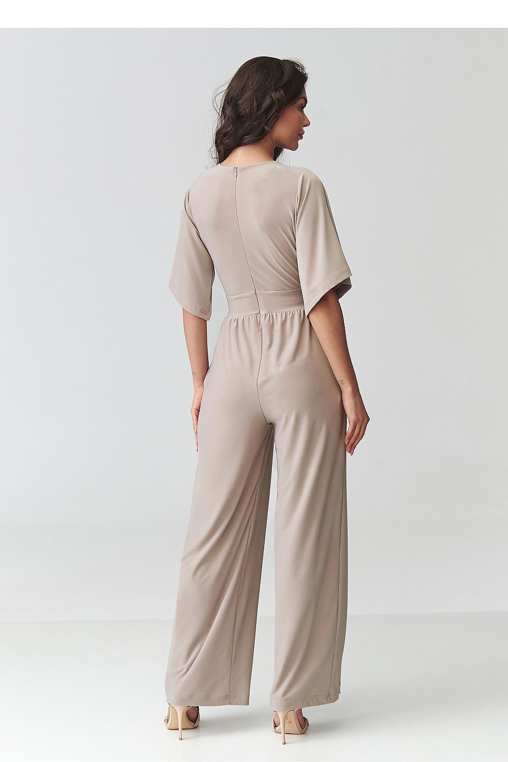Woman wearing a beige jumpsuit on a plain background