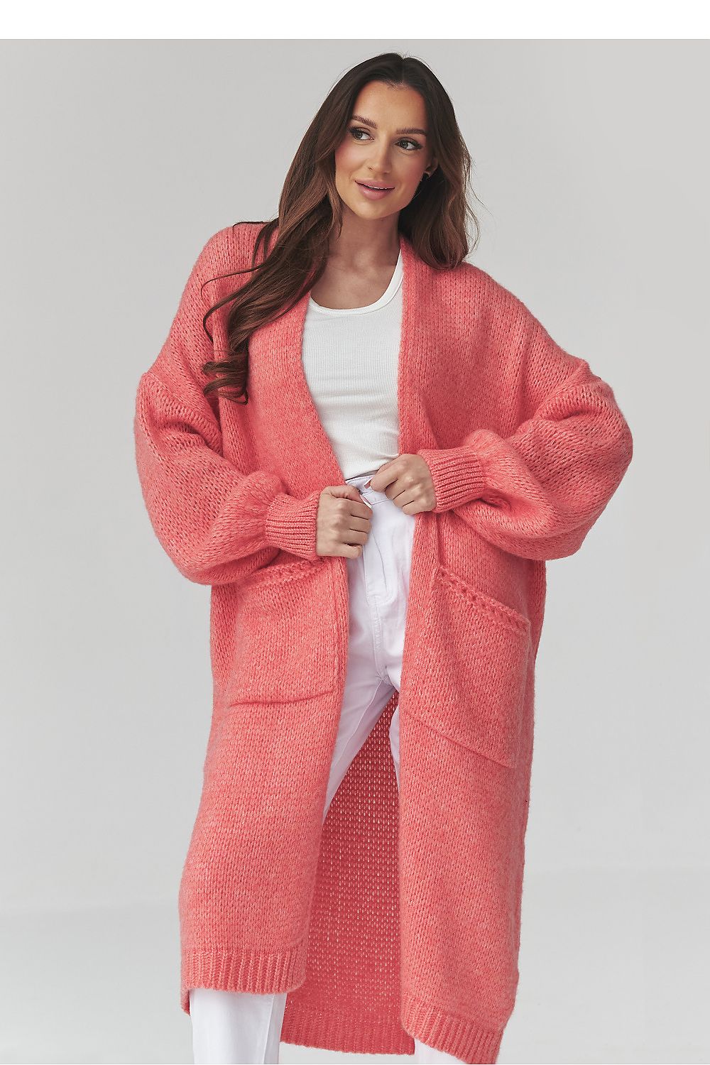 Woman wearing a long coral cardigan over a white top on a light gray background