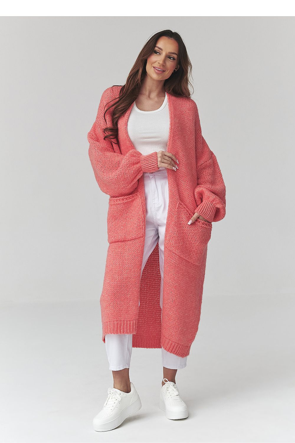 Woman wearing a long pink cardigan over a white outfit on a light gray background