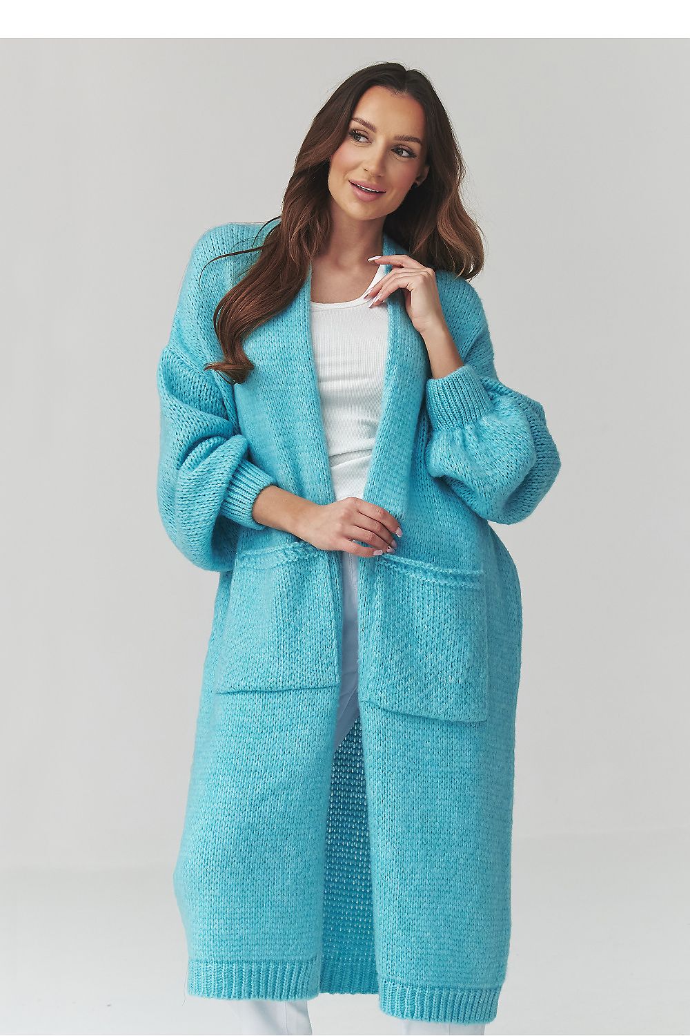 Woman wearing a long blue knitted cardigan on a light gray background